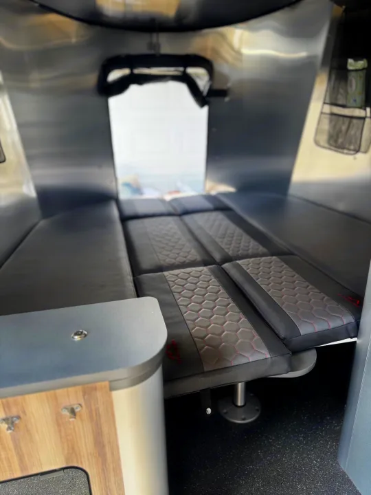 RV rental interior showing a convertible bed with gray/black hexagonal patterned cushions and sleek silver walls.. Airstream Basecamp 2021