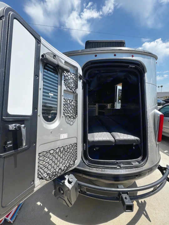 This silver RV rental's open rear hatch reveals a compact interior with seating, ready for adventure.. Airstream Basecamp 2021