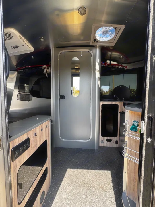 RV rental interior: modern kitchen, AC unit, vent fan, and connecting cabin door, with wood-look cabinetry.. Airstream Basecamp 2021