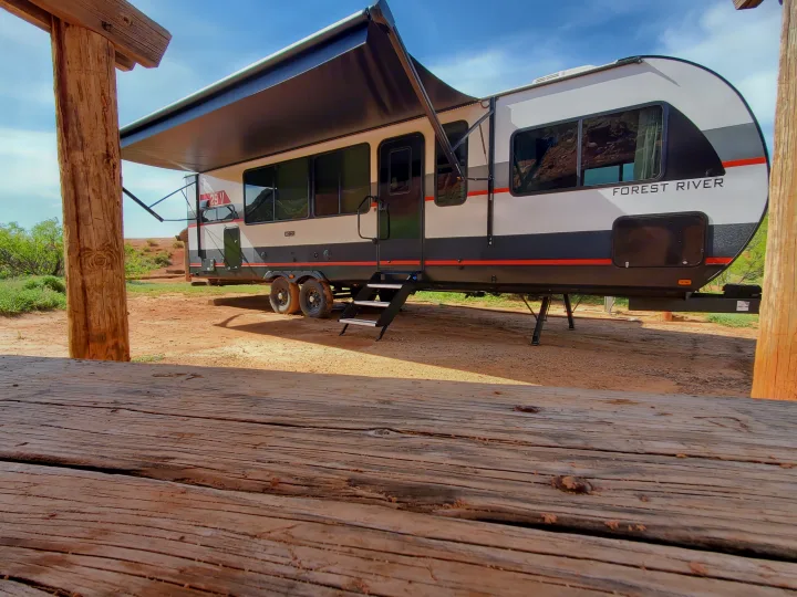 A Forest River RV rental with its awning extended, parked on dirt near a picnic table in a desert landscape.. Forest River Salem Platinum 2024