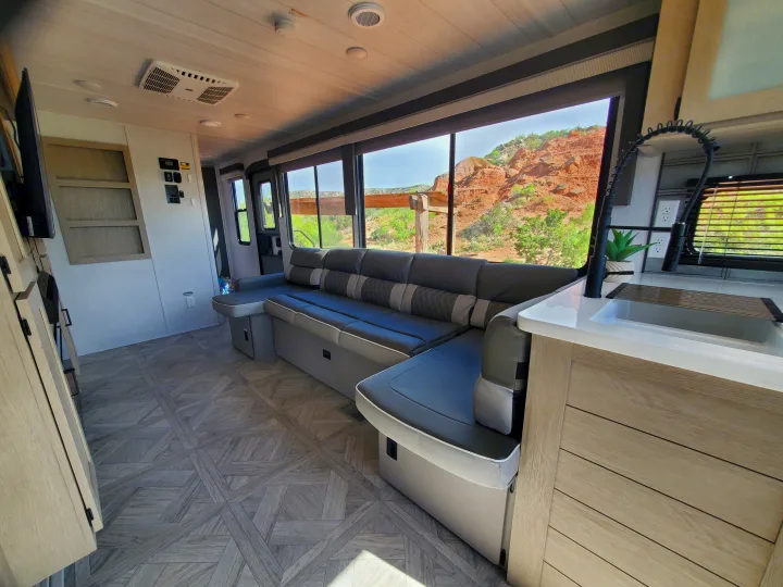 Bright RV rental interior showing a comfortable sectional sofa, kitchen area, and expansive windows with desert landscape views.. Forest River Salem Platinum 2024