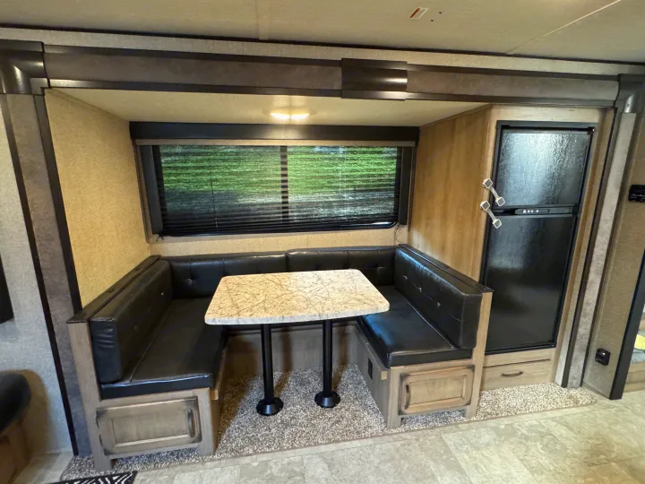RV rental interior featuring a spacious dinette with U-shaped black bench seating, a white table, and a refrigerator.. Grand Design Transcend Xplor 2020