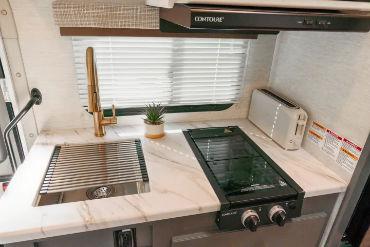 Well-equipped RV rental kitchen with a modern sink, golden faucet, stovetop, toaster, and elegant marble-look counters.. Thor Motor Coach Eddie Bauer 21EBF 2025