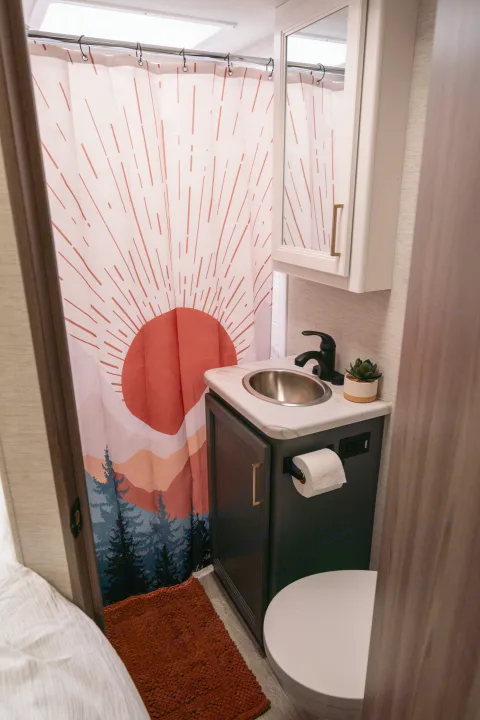 Compact RV rental bathroom: colorful shower curtain, round sink, vanity, toilet, and a cozy bath mat.. Thor Motor Coach Eddie Bauer 21EBF 2025