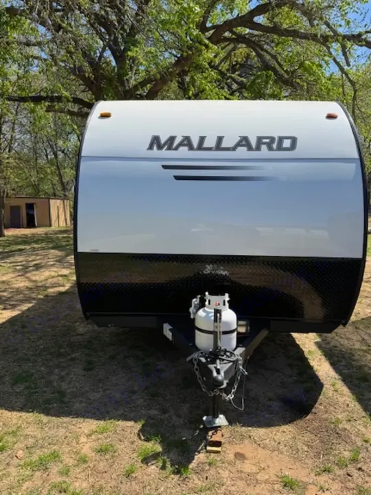 Front view of a white and black "Mallard" travel trailer with a propane tank, ideal for an RV rental.. Heartland Mallard Mallard 2025