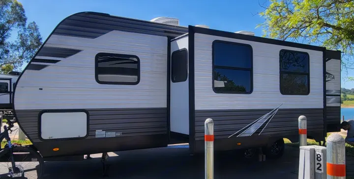 This RV rental, a grey and white travel trailer, is parked at a lakeside campsite, perfect for outdoor adventures.. Highland Ridge RV Olympia 2022
