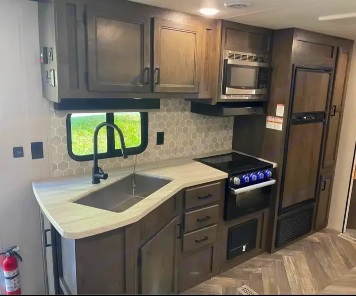 Modern RV rental kitchen with dark cabinets, light counter, sink, microwave, stove, and fridge visible on the right.. Highland Ridge RV Olympia 2022