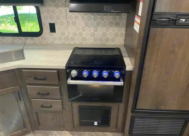 Modern RV rental kitchen with blue-lit stove knobs, oven, refrigerator, and stylish hexagonal backsplash.. Highland Ridge RV Olympia 2022