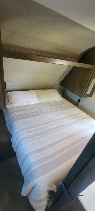 RV rental bedroom: a neat bed with striped bedding, textured headboard, and compact overhead storage.. Highland Ridge RV Olympia 2022
