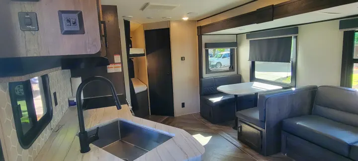 Modern RV rental interior features a kitchen sink, dinette with seating, a sofa, and bunk beds, ideal for comfortable travel.. Highland Ridge RV Olympia 2022
