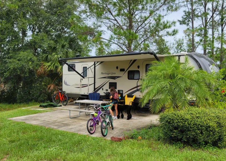 RV rental: A travel trailer set up at a green campsite with a girl, black dog, bikes, and picnic table.. Forest River Wildwood Heritage Glen Lite 2014