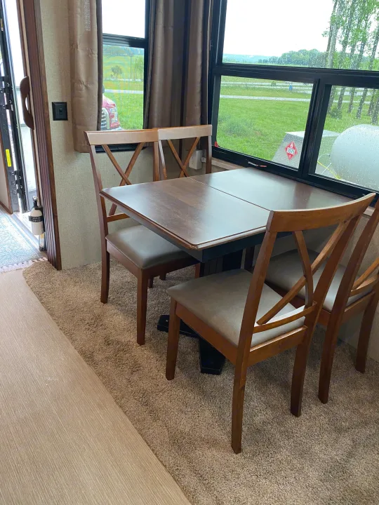 Inside an RV rental: a comfortable dining area with a wooden table and chairs, overlooking a green landscape.. Keystone RV Avalanche 2017