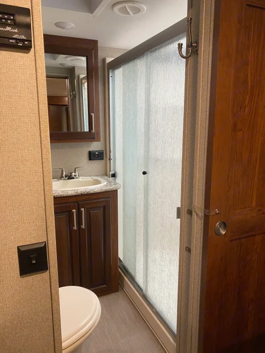 This RV rental bathroom features a functional vanity with a sink and mirror, a toilet, and a spacious frosted glass shower.. Keystone RV Avalanche 2017