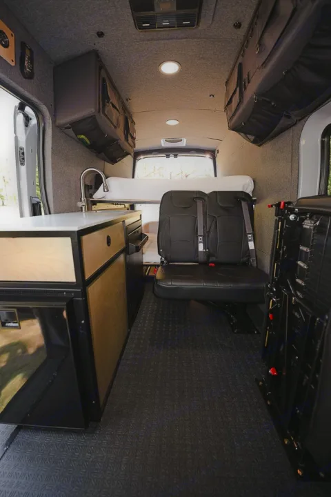 Spacious RV rental camper van interior showcasing a kitchen counter, cozy bed, and rear passenger seats.. Ford Transit 250 2023