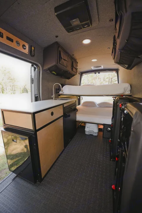 This RV rental camper van interior features a compact kitchen, bunk beds, and clever overhead storage, creating an efficient mobile living space.. Ford Transit 250 2023