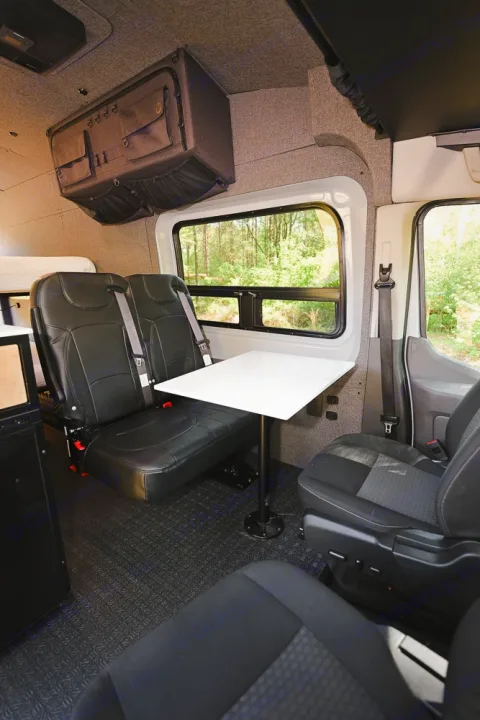 RV rental interior: two rear seats, a removable table, and overhead storage. Ideal for comfortable travel & adventures.. Ford Transit 250 2023