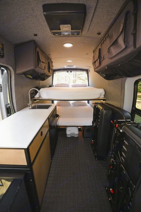 RV rental: Camper van interior with bunk beds, kitchen, storage, and folded seating. Carpeted floor, ceiling lights.. Ford Transit 250 2023