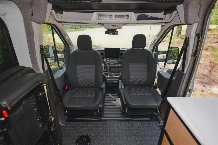 RV rental's front interior: two seats, dashboard, and clear view of an outdoor natural setting.. Ford Transit 250 2023