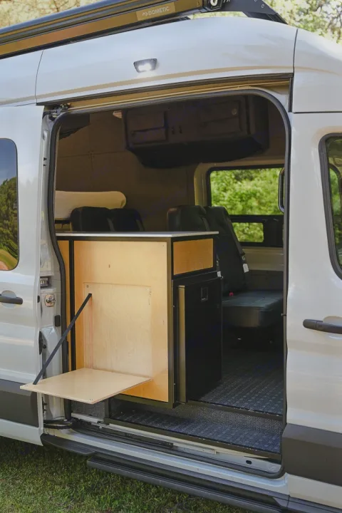 RV rental: Inside a camper van, a custom wooden counter with a fold-down table and fridge optimizes space for travel.. Ford Transit 250 2023