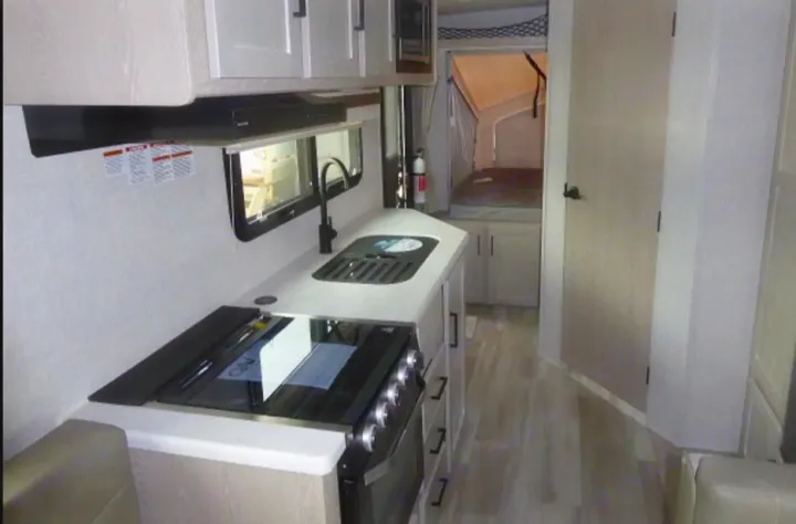 Spacious rv rental interior featuring a modern kitchen with stove, sink, and cabinets, leading to a comfortable sleeping area.. Rockwood Roo19 2022