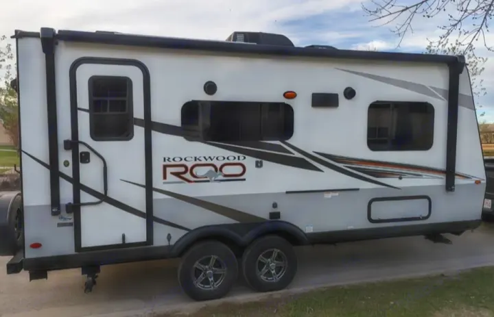 White Rockwood Roo travel trailer parked outdoors. This spacious RV rental is ideal for family camping and road trips.. Rockwood Roo19 2022