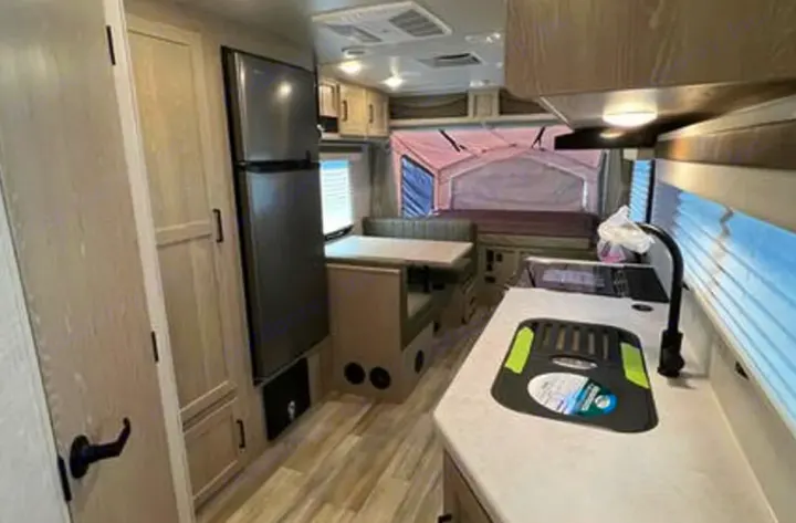 Spacious rv rental interior: kitchen with sink, fridge, dining area, and pop-out bed. Ready for adventure.. Rockwood Roo19 2022