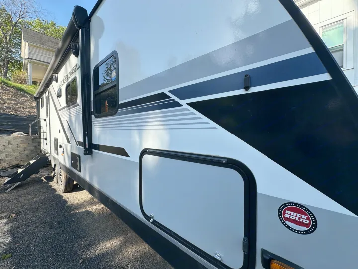 Side view of a white Jay Feather travel trailer RV rental, featuring an awning, windows, and stylish gray/black decals.. Jayco Jay Feather 2024