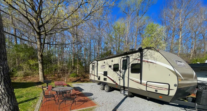 Travel trailer RV rental parked at a peaceful campsite with patio, grill, and nature. Ideal outdoor getaway.. Dutchmen Coleman Light LX 2018