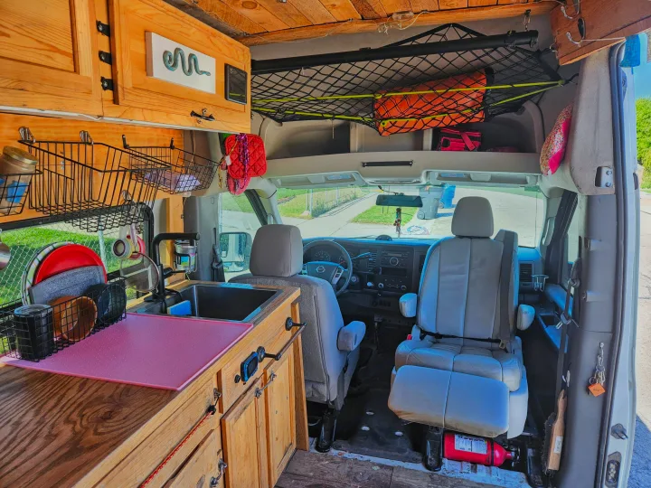 Cozy RV rental camper van interior with kitchen, storage, and driver's cabin view.. Nissan Other 2012