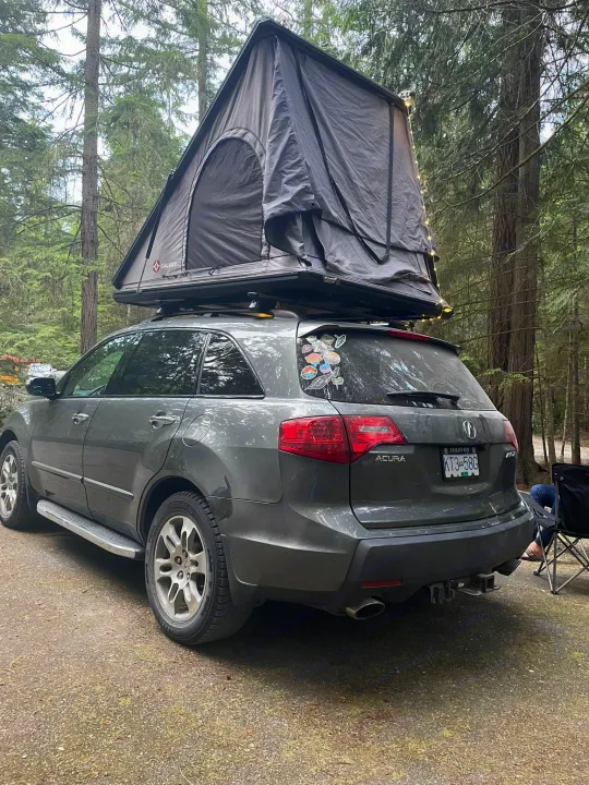 Gray Acura SUV with a deployed Galaxy rooftop tent in a forest campsite. An ideal RV rental alternative for your outdoor adventures.. Other Other 2007