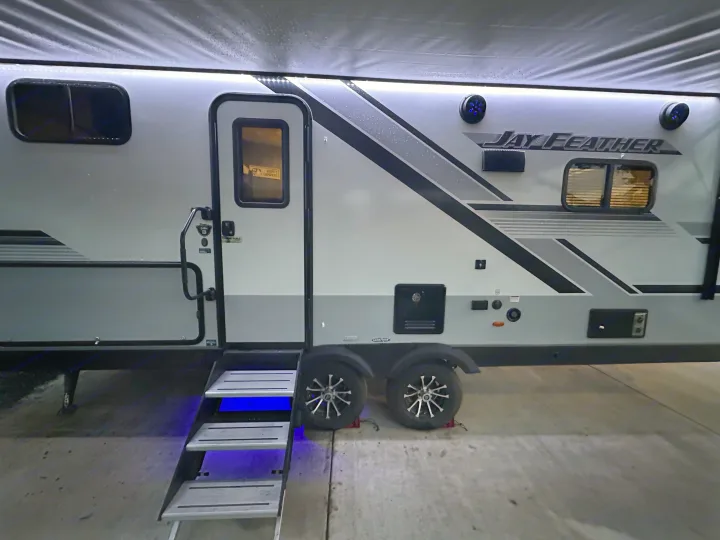 Jay Feather rv rental: a grey travel trailer with bright LED awning lights and blue-lit entry steps.. Jayco Jay Feather 2024