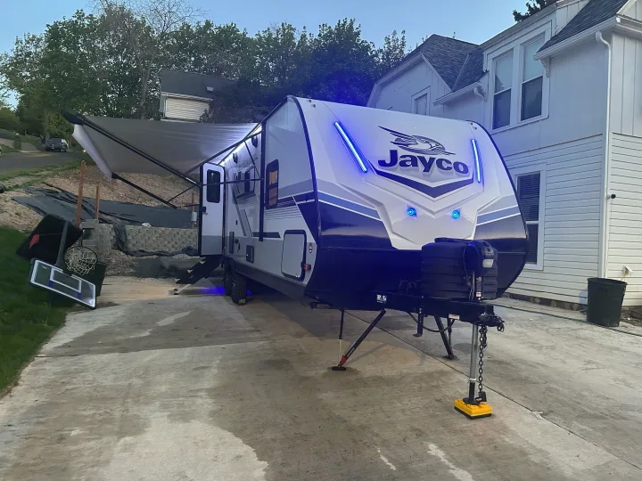 Jayco travel trailer RV rental parked at home with awning extended, glowing with blue lights at dusk, ready for camping.. Jayco Jay Feather 2024