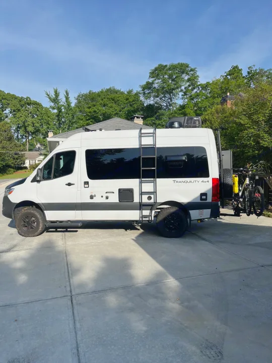 RV rental: White Tranquility 4x4 camper van with bikes, ladder, rooftop AC, parked on a driveway.. Thor Tranquility 2023