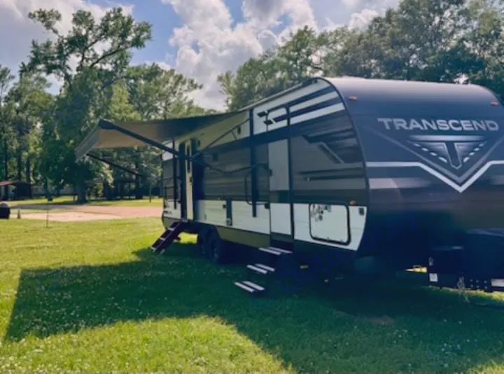 Experience outdoor adventure! This modern Transcend travel trailer RV rental is set up at a scenic campsite with its awning extended.. Grand Design Transcend Xplor 2022