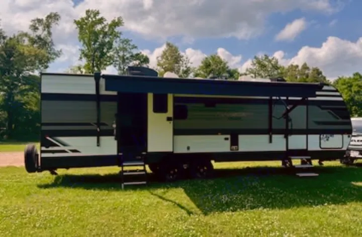 Spacious, modern travel trailer RV rental, white and dark green, with awning extended, parked on a grassy site for camping adventure.. Grand Design Transcend Xplor 2022