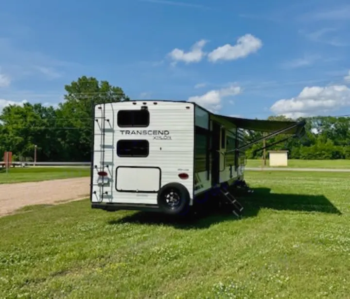 White Transcend XPLOR RV rental parked in a sunny grassy field with extended awning. Ready for your outdoor adventure!. Grand Design Transcend Xplor 2022