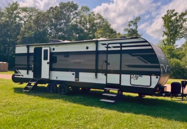 Spacious white & gray travel trailer RV rental, with steps down from the open door, parked on green grass under a blue sky.. Grand Design Transcend Xplor 2022