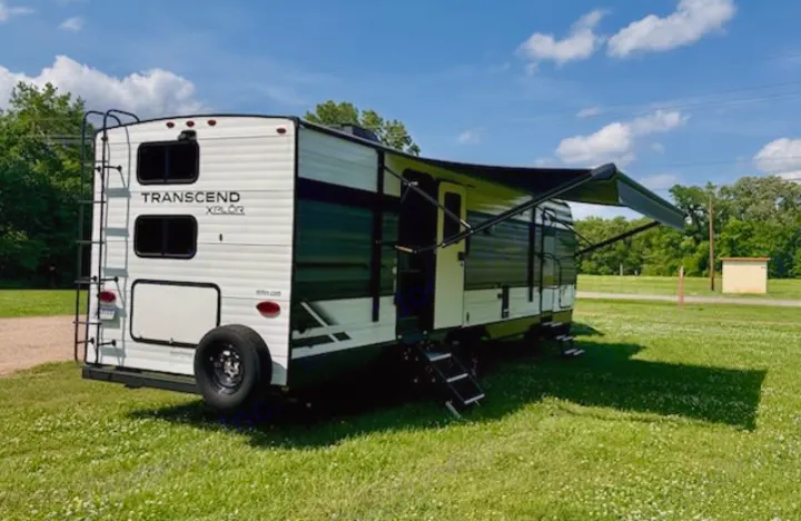 Ready for an RV rental adventure, this white Transcend Xplor travel trailer extends its awning in a sunny field.. Grand Design Transcend Xplor 2022