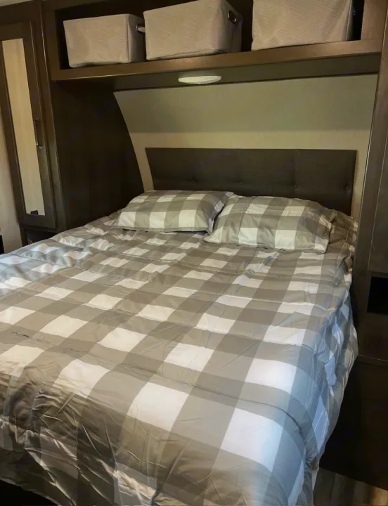 Cozy RV rental bedroom with plaid bedding, a comfy headboard, and handy overhead storage bins.. Grand Design Transcend Xplor 2021
