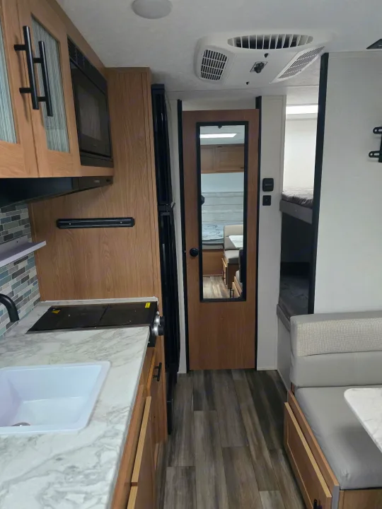 Spacious RV rental interior with a modern kitchen, comfortable dining booth, and convenient bunk beds for your travels.. Prime Time Avenger LT 16BH 2023