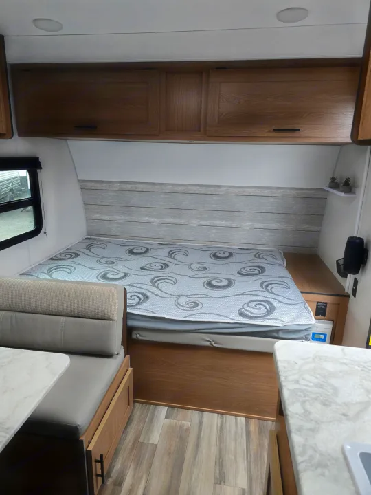 RV rental interior shows a cozy bed with patterned cover, wood cabinets, and dinette seating, perfect for travel.. Prime Time Avenger LT 16BH 2023