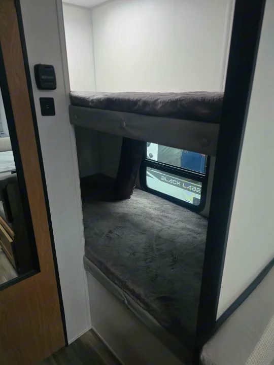 This RV rental features comfortable bunk beds with soft grey bedding, ideal for family travel. Charging port & thermostat visible.. Prime Time Avenger LT 16BH 2023