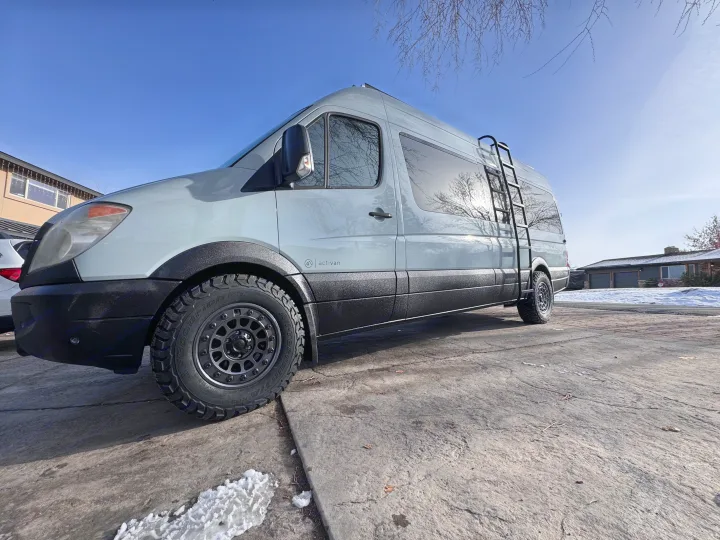 Light grey activan camper van with off-road tires & ladder, parked on a sunny driveway. Perfect rv rental adventure awaits!. Mercedes-Benz Sprinter RV Motorhome Campervan 2012