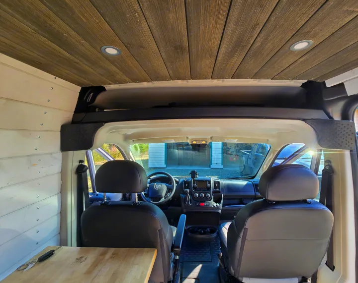 Custom RV rental camper van interior featuring wooden plank ceiling, white paneled walls, and the front driver's area.. Ram Promaster 2020