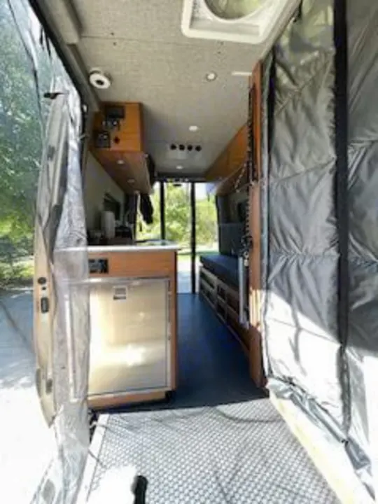 Step into this custom RV rental camper van! Interior view from rear shows kitchen, bed, and open screened doors to the outside.. Mercedes-Benz Sprinter RV Motorhome Campervan 2020