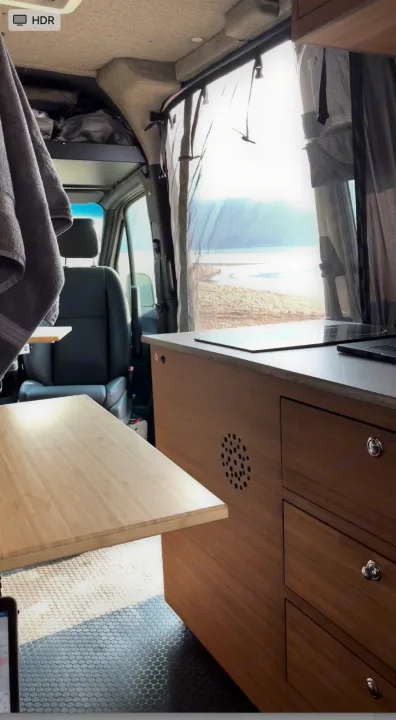 RV rental interior with a bright beach view, showing a compact kitchen, pull-out table, and integrated storage.. Mercedes-Benz Sprinter RV Motorhome Campervan 2020