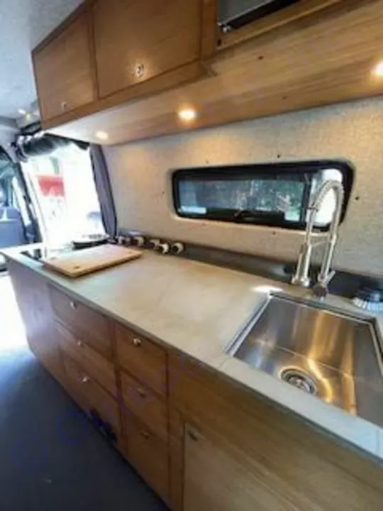 Explore this modern RV rental kitchen featuring a sink, wood cabinets, and ample counter space, ideal for your next van life adventure.. Mercedes-Benz Sprinter RV Motorhome Campervan 2020