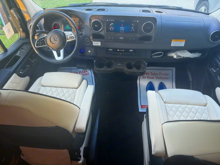 View of the interior of a Mercedes-Benz rv rental, featuring the modern cockpit, dashboard, steering wheel, and plush white seats.. Mercedes-Benz Sprinter 2025