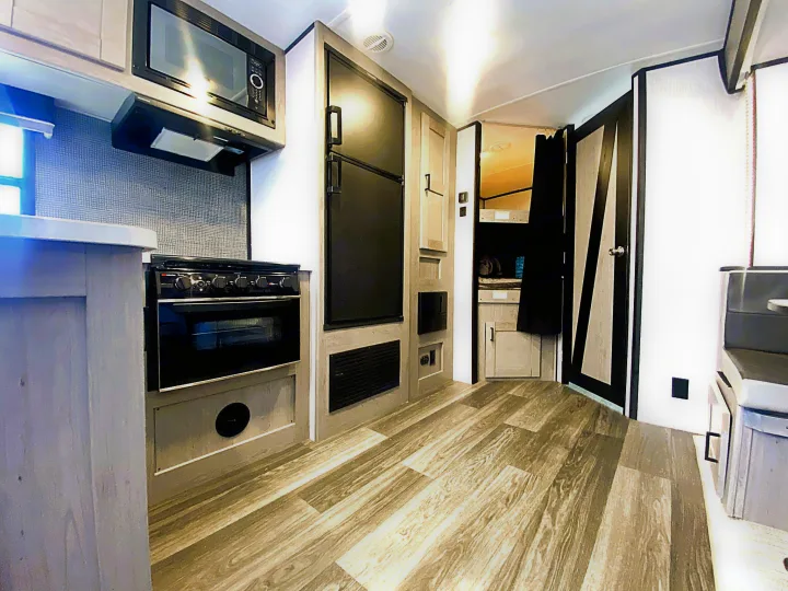 Step into this modern RV rental kitchen. Features microwave, stove, fridge, light wood flooring. Bunk beds visible for your adventure.. Heartland RVs Mallard 2021