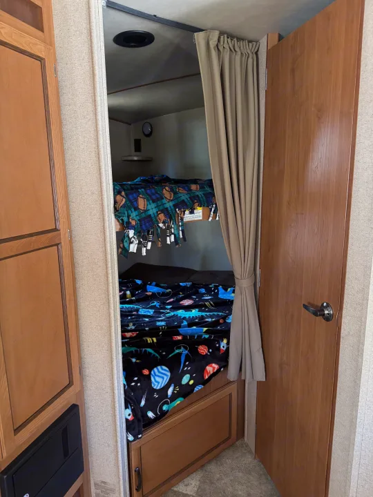 Cozy bunk beds in an RV rental, with fun themed blankets, a pulled-back privacy curtain, and wood interior.. Crossroads RV Sunset Trail Super Lite 2017